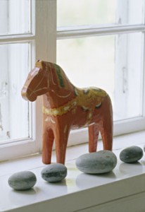 A detail of a carved, painted wooden horse, a collection of stones placed on a window sill,