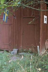A detail of the exterior of a wooden country house set amongst trees and shrubs,